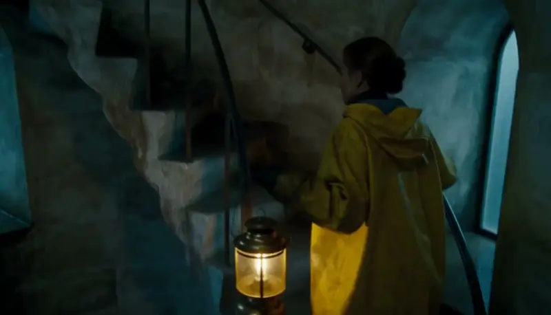 A lighthouse keeper in a yellow coat climbs a stone spiral staircase holding a lit lantern